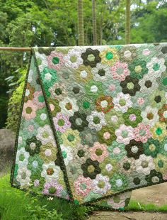 a quilt hanging on a clothes line in the grass with trees in the back ground