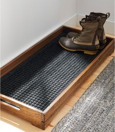 a pair of hiking boots sitting on top of a wooden floor mat next to a rug