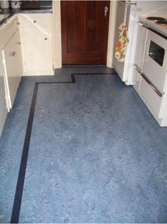 an empty kitchen with blue flooring and white appliances in the back ground, next to a wooden door