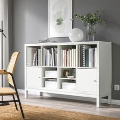 a white bookcase with many books on it and a chair in front of it