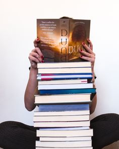 a woman sitting on the floor holding up a stack of books