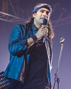 a man holding a microphone in his right hand and wearing a turban on top of his head