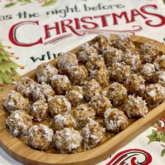 a wooden platter filled with snowball cookies on top of a table next to a christmas sign