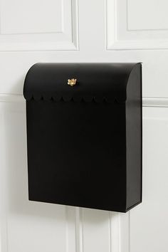 a black mailbox mounted to the side of a white door with scalloped edges