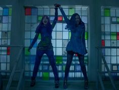 two young women standing in front of colorful glass blocks with their hands up and arms outstretched