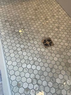 a white bathroom with hexagonal tiles on the floor and shower head in the middle