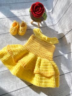 a crocheted baby dress and booties are sitting on a white surface next to a red rose