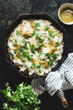 a dish with broccoli, cheese and sauce in it on a table next to some parsley