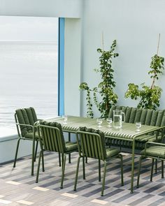 an outdoor dining table with green chairs and potted plants next to the water's edge