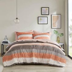 a bed with orange and grey striped comforter in a room next to a window