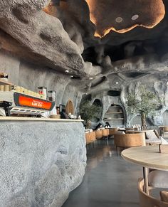 a restaurant with tables and chairs in front of a rock wall that looks like it has been built into the ceiling