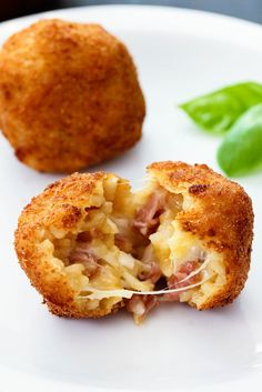 a white plate topped with meat and cheese covered pastries next to green leafy leaves