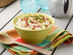 a green bowl filled with food sitting on top of a table next to a wooden spoon