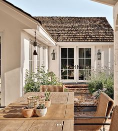 a wooden table sitting on top of a patio next to a white house with french doors