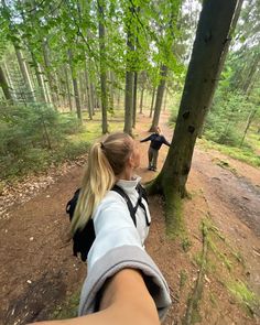 two people are walking in the woods with backpacks on and one person is holding out their hand