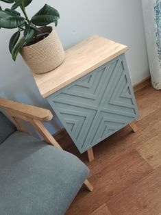 a plant sitting on top of a wooden cabinet next to a gray chair and potted plant