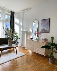 a living room filled with furniture and potted plants on top of a hard wood floor