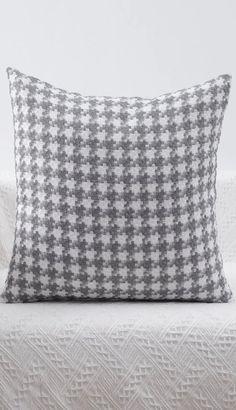 a gray and white pillow sitting on top of a bed next to a white wall