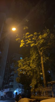 a person sitting on the ground under a street light at night with buildings in the background