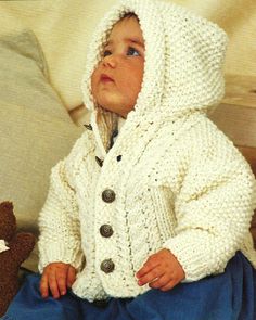 a baby wearing a white knitted jacket and hat