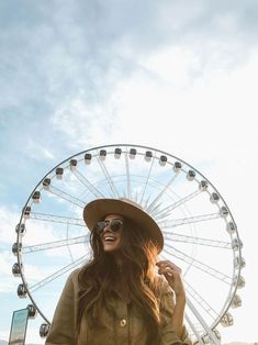 a woman standing in front of a ferris wheel wearing sunglasses and a hat with her hand on her hip