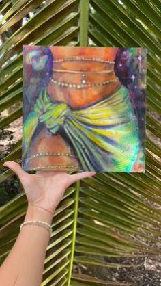 a woman holding up a painting in front of a palm tree