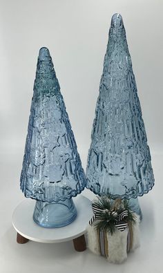 two blue glass christmas trees sitting on top of a white plate next to each other