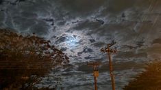 the full moon shines brightly in the cloudy sky above power lines and telephone poles