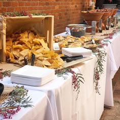 a table with food on it is set up in front of a brick wall and some potted plants