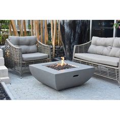 a fire pit sitting on top of a patio next to two chairs and a table