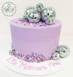 a purple cake with silver disco balls on top and confetti around the edges