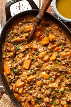 a skillet filled with beans and vegetables next to a bowl of soup on a wooden table