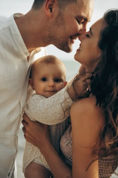 a man and woman are holding a baby on the beach while smiling at each other