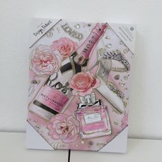 a card with pink flowers and perfume bottles on it, sitting next to a white wall