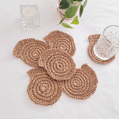 four woven coasters on a white tablecloth with a vase and glass in the background