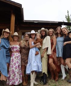 a group of women standing next to each other in front of a wooden building with cowboy hats on