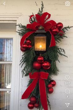 a christmas wreath hanging on the side of a white building with red ornaments and a lit candle