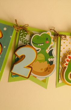 two birthday cards hanging on a wall with the number two in front of them and an image of a dinosaur