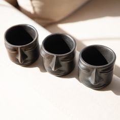 three black vases sitting on top of a white cloth covered table next to each other