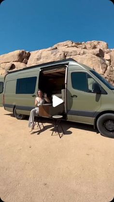 a woman sitting at a table in front of a van with the door open and windows open