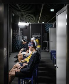 several people sitting on blue chairs in a room with black walls and white ceilinging