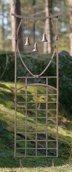 an iron gate with three bells hanging from it's sides in the grass next to some trees