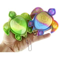 two small turtle keychains in the palm of a person's hand, one is multicolored