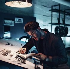 a man sitting at a table writing on a piece of paper while holding a pen