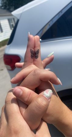 two people holding each other's hands with butterfly tattoos on their thumb and fingers