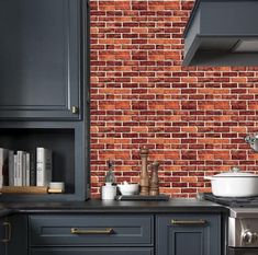 a kitchen with black cabinets and red brick wall behind the stove top oven is shown