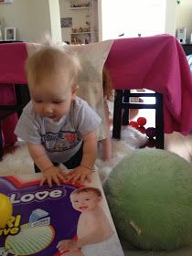 a baby playing with a book on the floor next to a green ball and chair