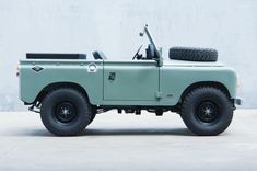 an old green truck parked in front of a white wall with two tires on it