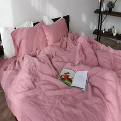 a book is laying on top of a pink comforter in a bedroom with white walls