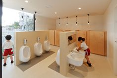 two children playing in a public restroom with urinals and sinks on the walls